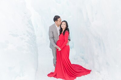 Red dress maternity session husband kisses wife temple in ice castle, Dillon, CO
