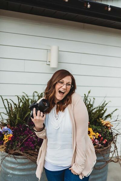 woman holding camera and smiling in front of flowers