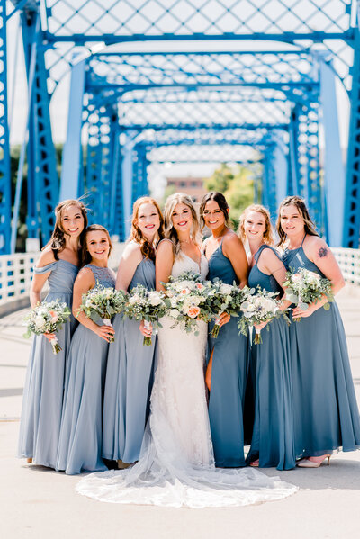 Group of bridesmaids on Grand Rapids blue bridge holding white and peach floral bouquets by Grand Rapids wedding photographer Stephanie Anne