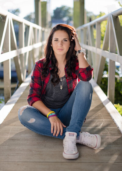 high school senior girl in jeans and red flanel seated on bridgeway path