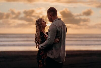 A couple standing in the sunset light at the beach during their engagement photoshoot with Tashina Narelle
