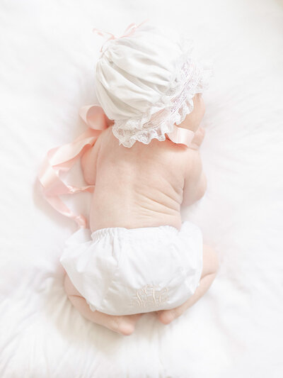 Newborn Baby lying on stomach sleeping wearing an heirloom bonnet and monogrammed bloomers