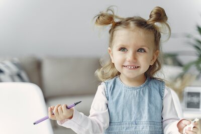 white preschool girl in pigtails wearing denim jumper writing