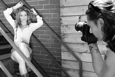 Behind the scenes black and white Mark Maryanovich photographing musician Mandy Bo sitting on metal staircase arms above head next to brick wall