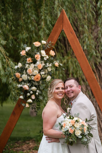 bride and groom smiling while hugging under the willow tree at barnwood events in madisioon, winconsin.