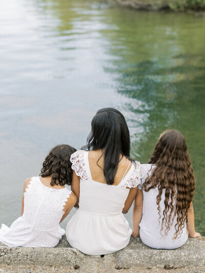 The back of a mom sitting down in between her two daughters as they are all dressed in white