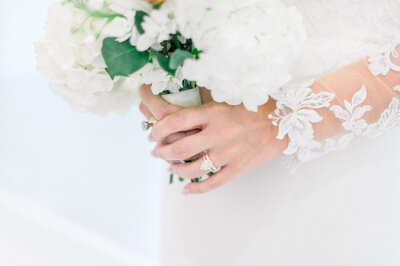 close up image of brides hands holding bouquet with long lace sleeves and white flowers