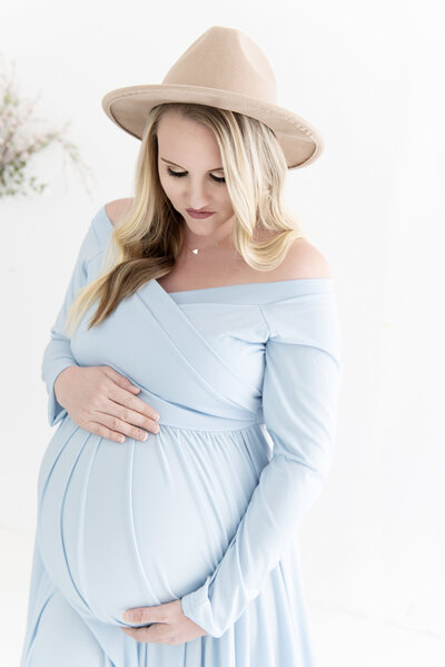 Stunning pregnant mom in a blue maternity gown and tan hat holding her bump posed by a Greater Atlanta Motherhood & Family Photographer