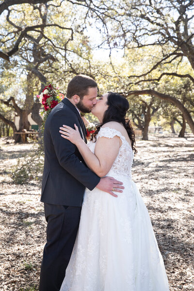 An Austin-based wedding photographer captures a bride and groom sharing a tender kiss in a picturesque wooded area.