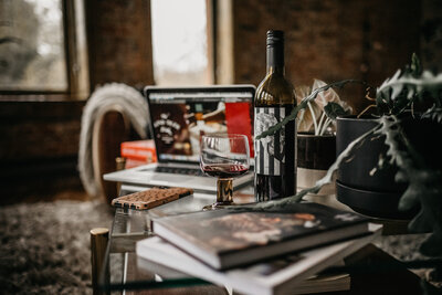 A coffee table with a luxury branding project on Clair Schwem's computer in the background. A casely phone case sits in front of a bottle of red wine.