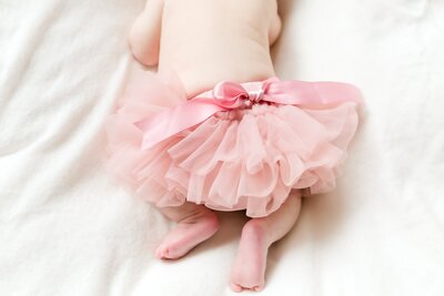 Baby wearing pink skirt lays on blanket.
