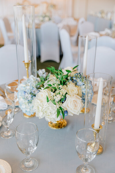 Ivory roses with blue hydrangeas in low centerpiece surrounded by glasses and gold details