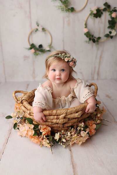 1 year old girl sitting in a basket wearing a boho dress and a flower halo
