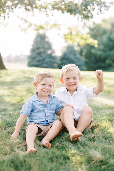 Two toddler brothers smile together in a field in Pennsylvania playing in the grass
