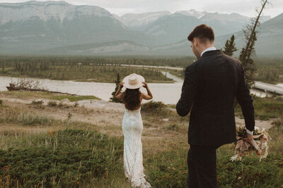 bride in white wedding dress with long train walking by river and mountains