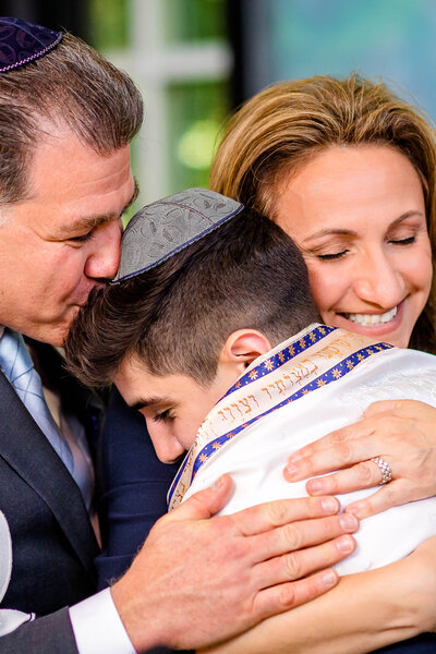 A mother and father celebrate their son's Bat Mitvah with a tender hug and kiss for him taken by a Bellevue Bar and Bat Mitzvah photographer