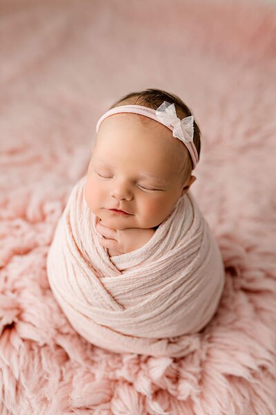 newborn baby girl wrapped in pink posed on a pink rug