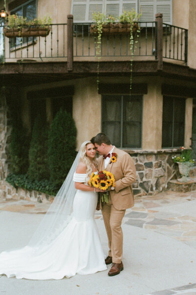 A romantic, documentary-style photograph capturing a bride and groom sharing a tender moment at Daniel Stowe Botanical Garden. This elegant wedding photography session highlights the couple's love amidst the lush, vibrant greenery of this beautiful venue.