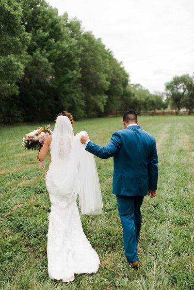 New Mexico based  Bride and Groom walking with the groom holding up the bride's veil in a grassy field.