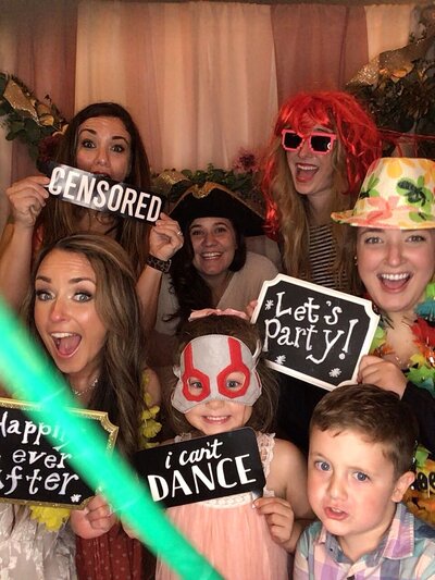 Group of 7 wedding guests in the photobooth dancing around laughing with props and signs