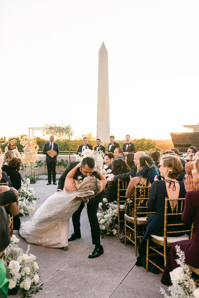 newlyweds dip kiss in aisle during rooftop ceremony at the American Histroy Museum in Washington, DC fine art wedding photography
