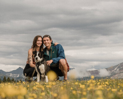 couple poses with their dog in a field of yellow flowers