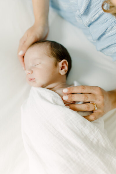A close up image of a mother holding her newborn baby boy's fingers while he lays swaddled during photo session with Boston newborn photographer Corinne Isabelle