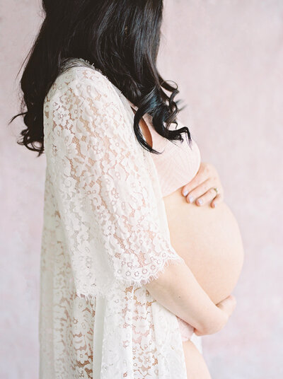 An expecting mother in a lace robe with black hair cradles her belly