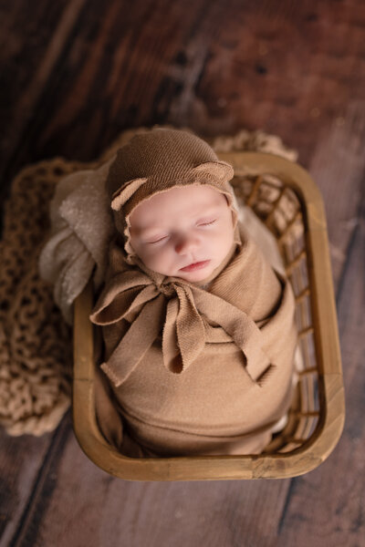A newborn baby in a brown blanket laying in a basket.