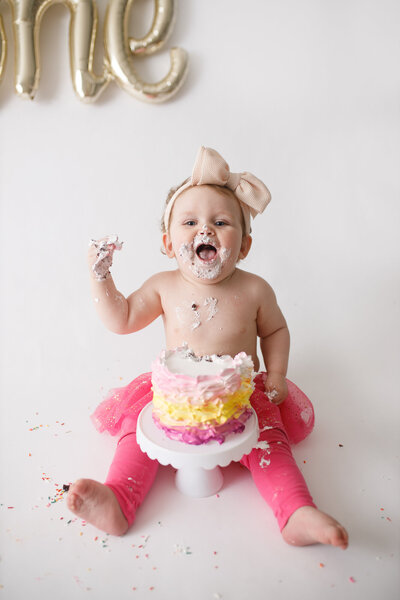 baby girl smiling while eating cake for 1st birthday in link tutu and leggings
