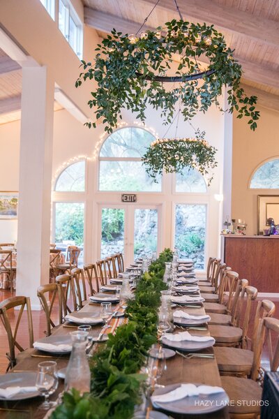 A long table with chairs and hanging greenery from the ceiling, creating a refreshing and inviting atmosphere.