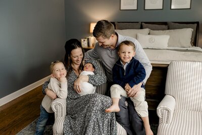 charlotte couple sits in their home with their two sons holding their newborn son  wearing blue neutral colors