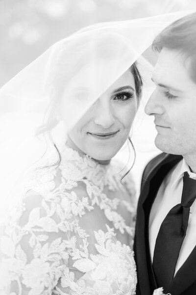 Black and white photograph of a bride and groom under the bride's wedding veil.