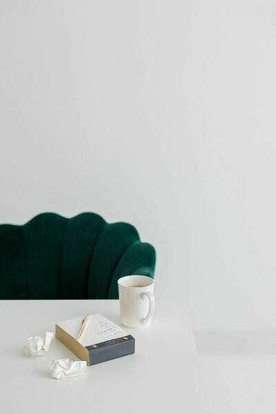 Green scalloped chair sitting behind a white table with a notepad and mug