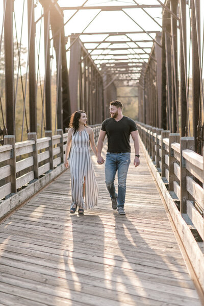 Couple holds hands while walking on a bridge