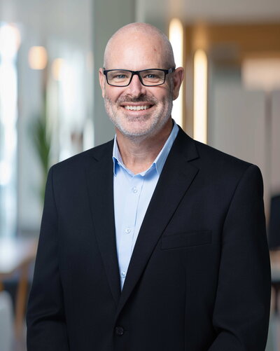 A person stands on stone steps in front of a large stone building, holding a bright red coat. They are wearing a white dress and red shoes. Trees are visible in the background.