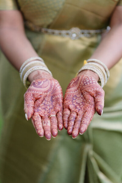 bride holds out her hands with Mehndi she wears a green saree