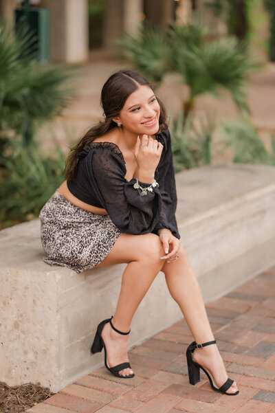 Girl in a black crop top and skirt leans forward and smiles off to the side during San Antonio senior pictures.