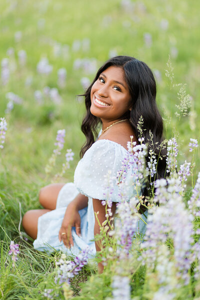 Girl sitting in a field of flowers, smiling.