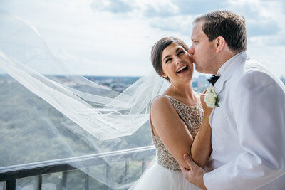 A bride and groom sharing a romantic kiss on a balcony overlooking the city captured beautifully by a Texas wedding videographer.