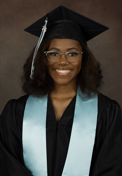 senior-girl-in-cap-and-gown-in-studio-with-brown-backdrop