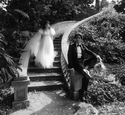 bride walking down the stairs while groom poses during a portrait session at Hycroft Manor Vancouver