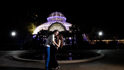 married couple kissing in front of a glass conservatory at night