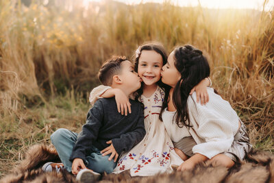 Family Photographer,  siblings on a blanket kissing each other at golden hour