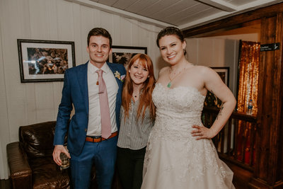 bride and groom smiling with woman standing between them