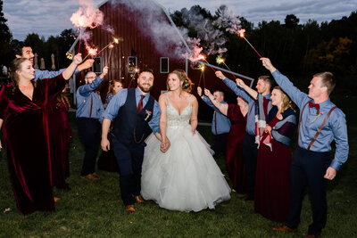 Bride and groom walking through sparkler exit in front of a red barn