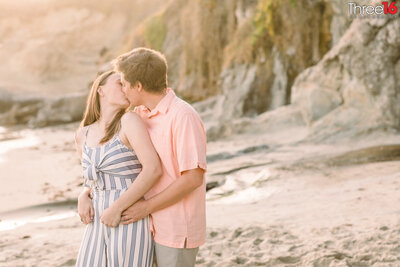 Bride to be looks back at her Groom as they share a kiss while he holds her from behind at Picnic Cove in Laguna Beach