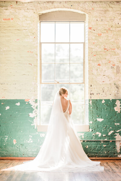 Bride Standing in front of distressed wall at The Engine Room in Monroe, GA in front of large window.