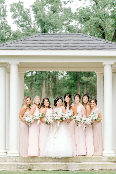Bride and bridesmaids pose with bouquets in outdoor gazebo