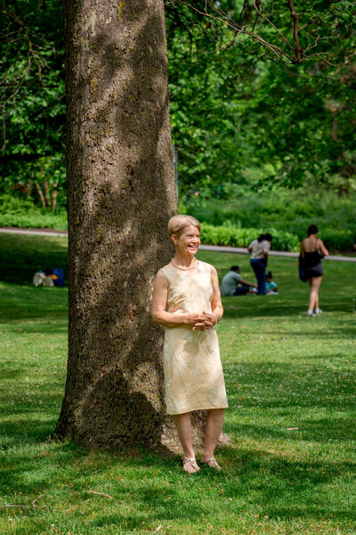 Guest in cream dress smiling while standing beside tree in park – photographed by wedding photographer Niko Coric – Lumen Clarity Media.\